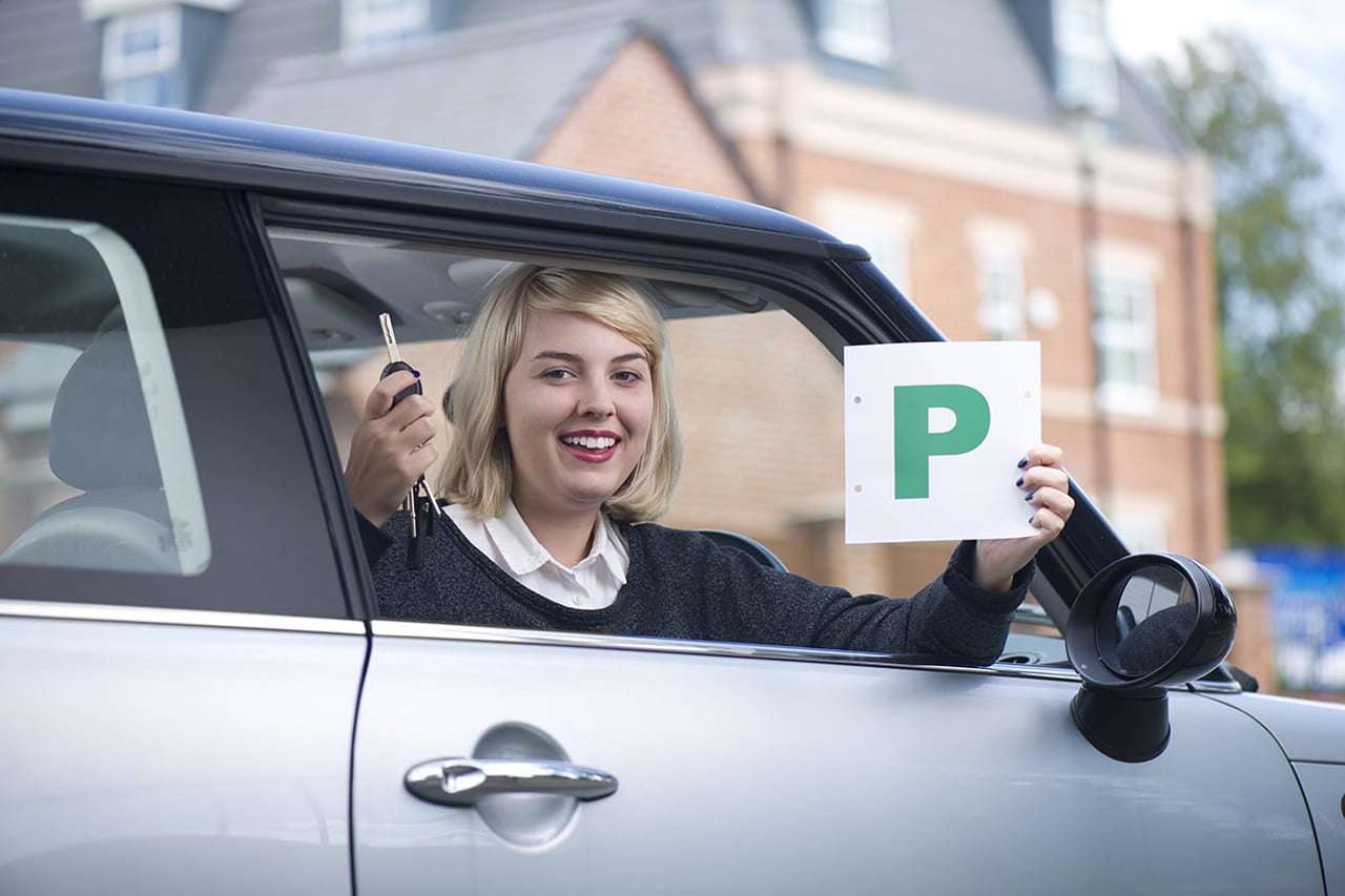 Female student sitting in the front of her car with her passed plate